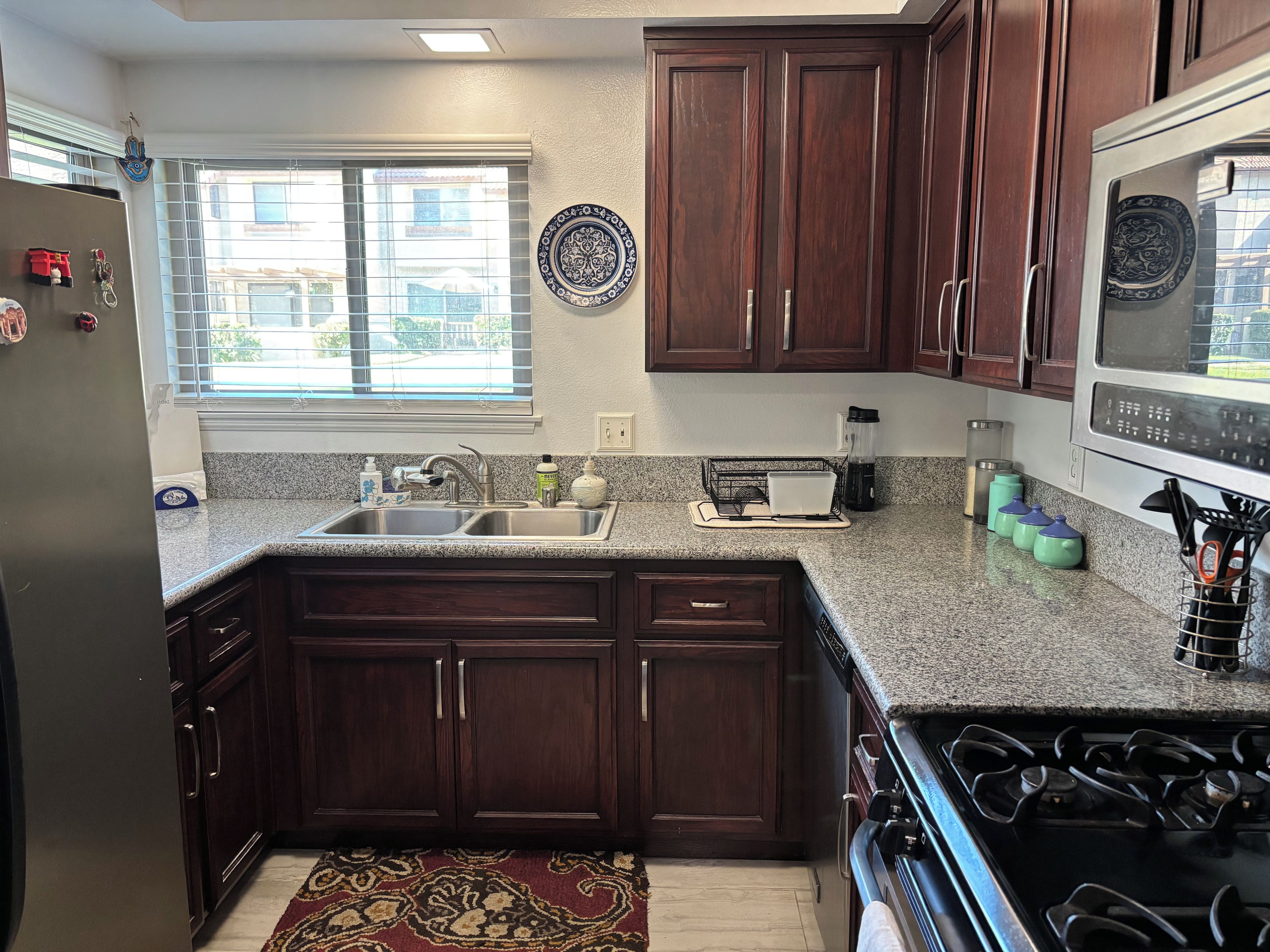 A kitchen with dark wood cabinets, a granite countertop, a stove, and a window with blinds.