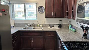 A kitchen with dark wood cabinets, a granite countertop, a stove, and a window with blinds.