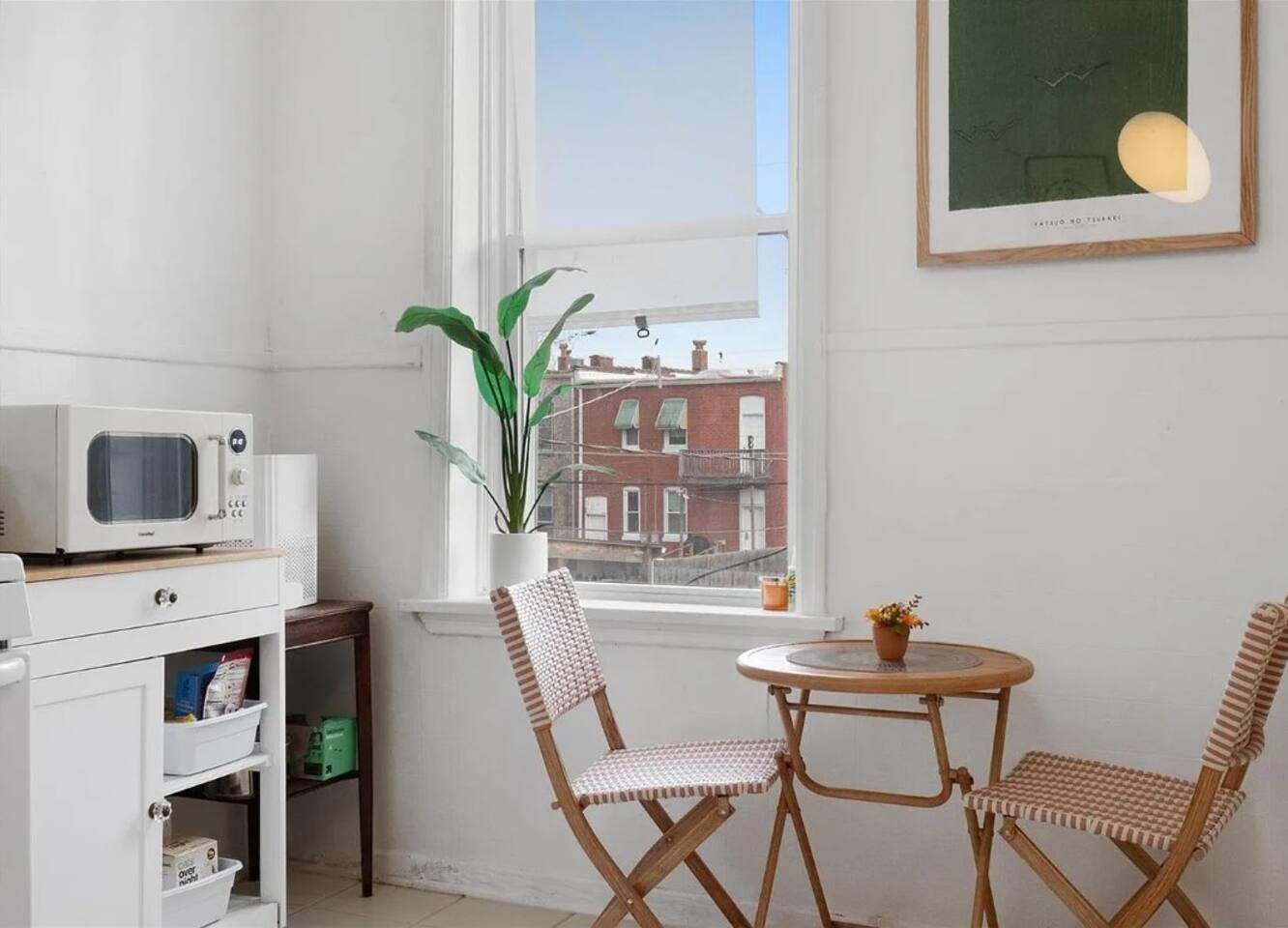 A small, bright room with a white microwave, a potted plant, two striped chairs, and a round table.