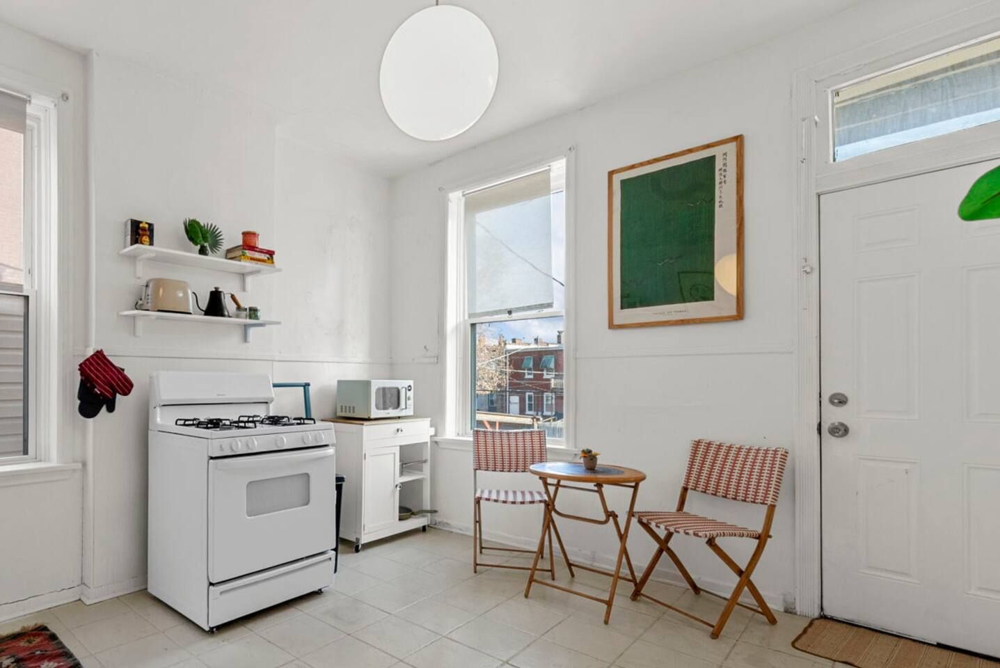 Une cuisine compacte équipée d’une cuisinière, d’un four à micro-ondes et d’étagères contenant des ustensiles de cuisine. On y trouve également un coin repas avec une table et des chaises, ainsi qu’une porte sur laquelle est posé un objet vert.