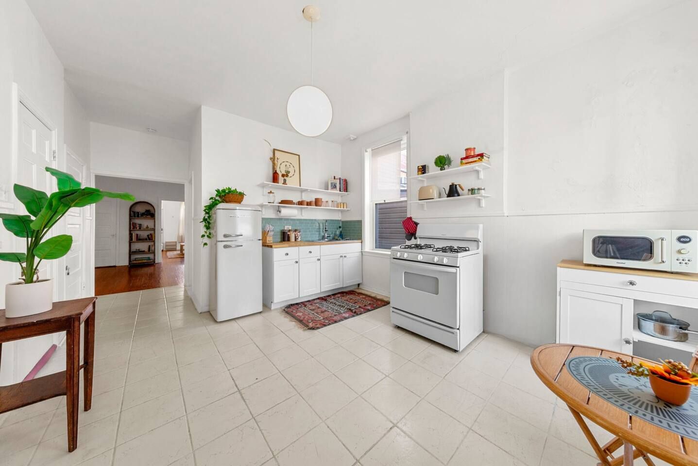 A modern kitchen with white cabinetry, a stove, a microwave, and a dining area with a table and chairs.