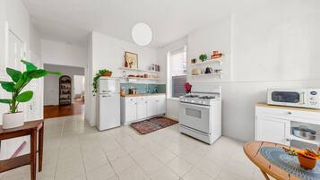 A modern kitchen with white cabinetry, a stove, a microwave, and a dining area with a table and chairs.