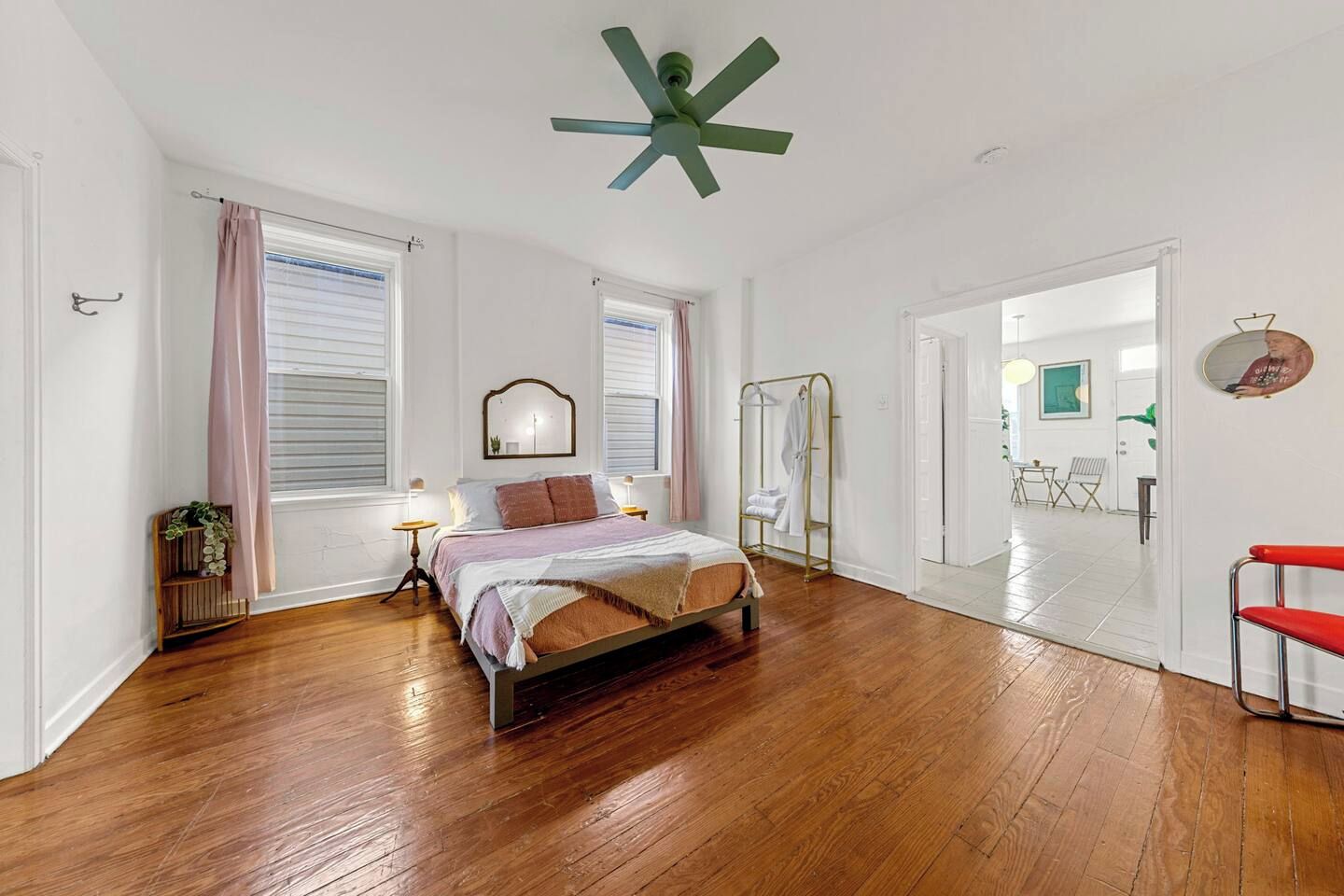 A spacious bedroom with a bed, bedside tables, a mirror, a wardrobe, and a red chair.