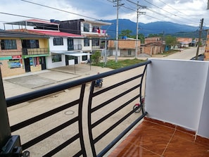 Un balcone con ringhiera metallica che si affaccia su una strada con edifici e una montagna sullo sfondo.