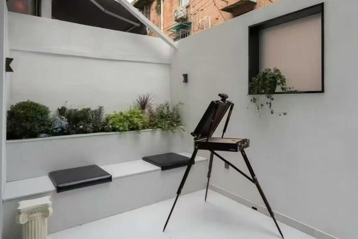 A minimalist room with a white wall, a small window, and a black chair.