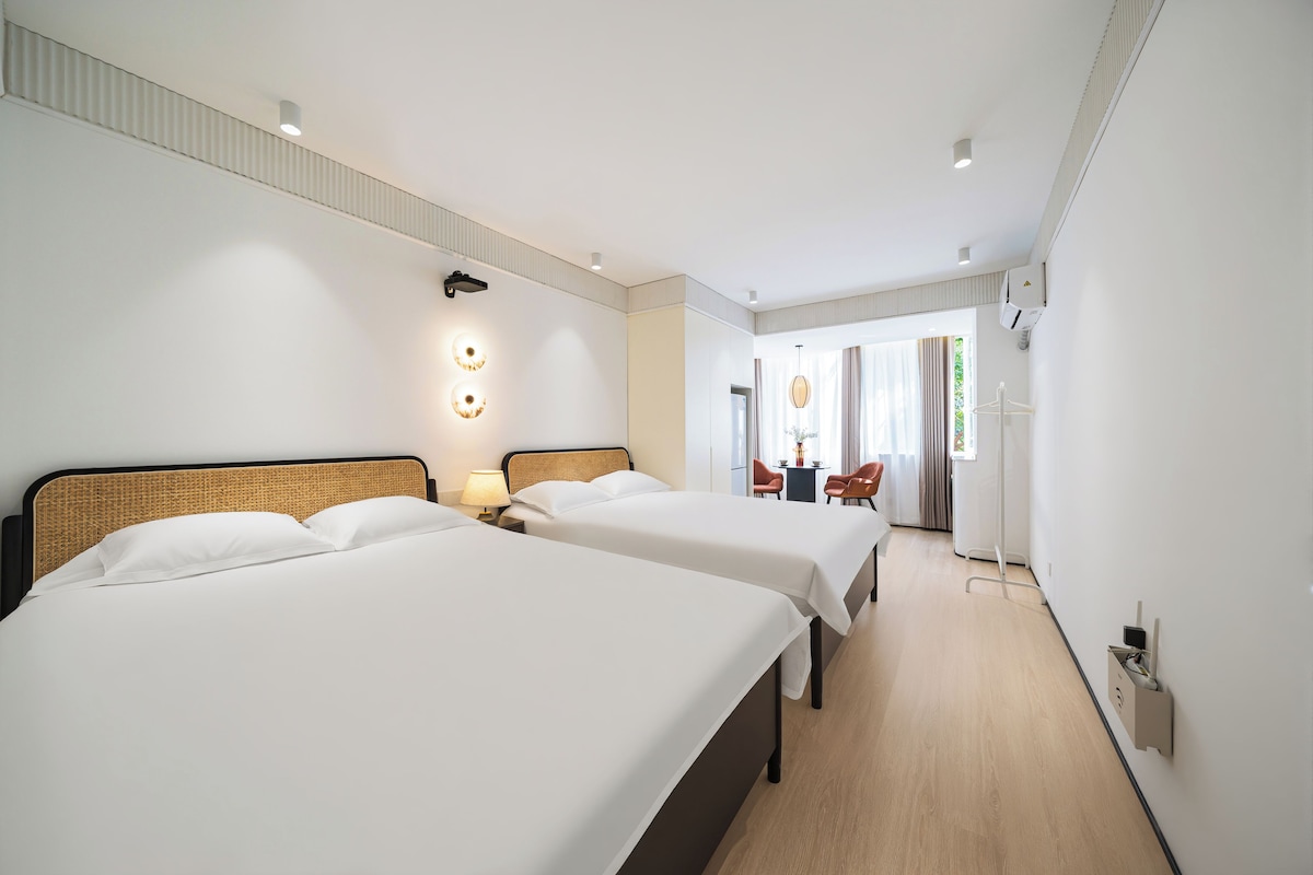 A hotel room with two beds, a sitting area with a table and chairs, and a view of the outdoors.