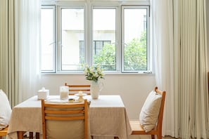 Un comedor con una mesa dispuesta para dos, un florero con flores, una vela y una caja de pañuelos.