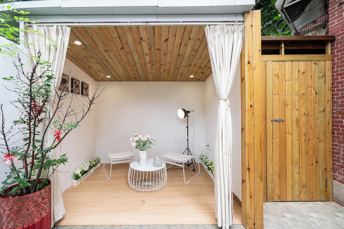 Un área de estar al aire libre y acogedora, con techo de madera, una puerta blanca y una planta en maceta.