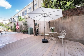 Une terrasse extérieure avec une table et des chaises, un grand parasol et un mur en briques.