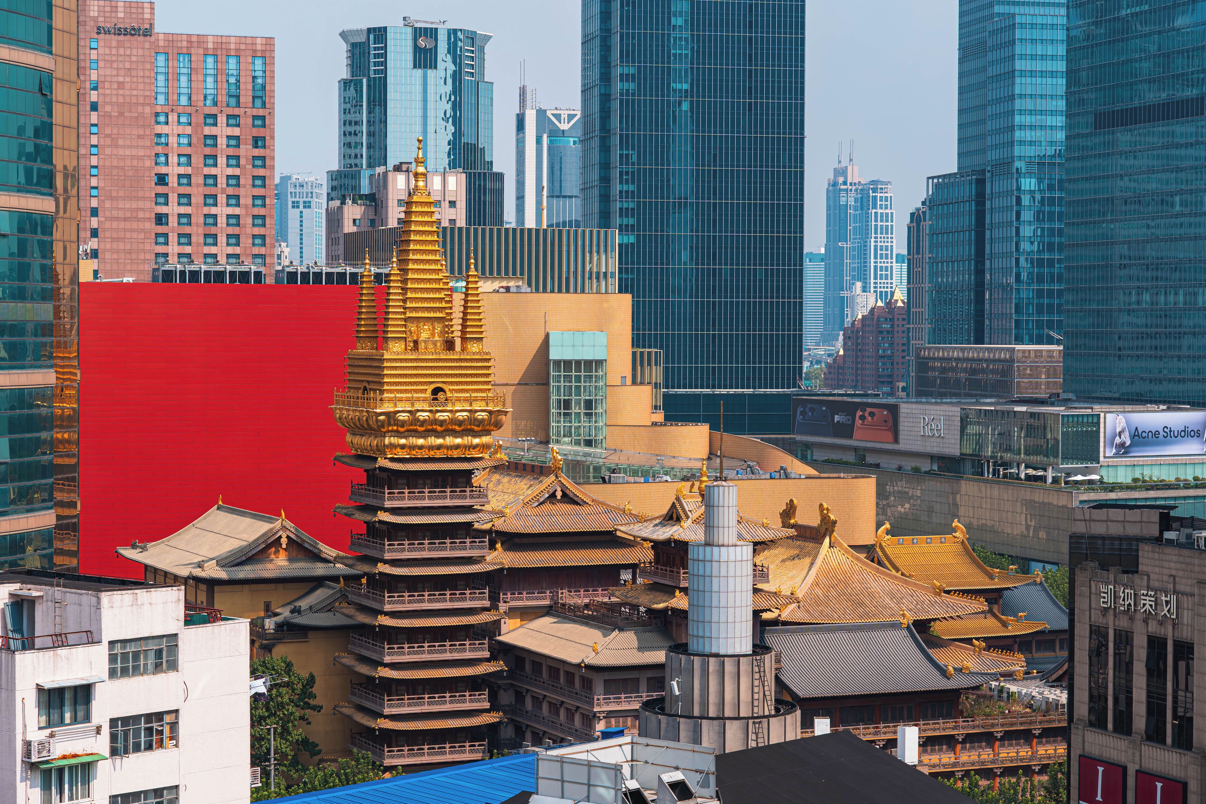 A traditional pagoda with multiple tiers and golden accents, surrounded by modern high-rise buildings.