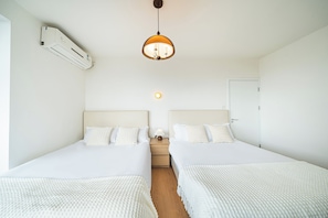 Et hotelværelse med to senge, en ventilator i loftet, en vægmonteret aircondition og en sengetårnlampe, samt en dør.