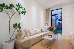 Un salon moderne avec un canapé, une table basse, une plante en pot et une vue sur l’extérieur grâce à une grande fenêtre.