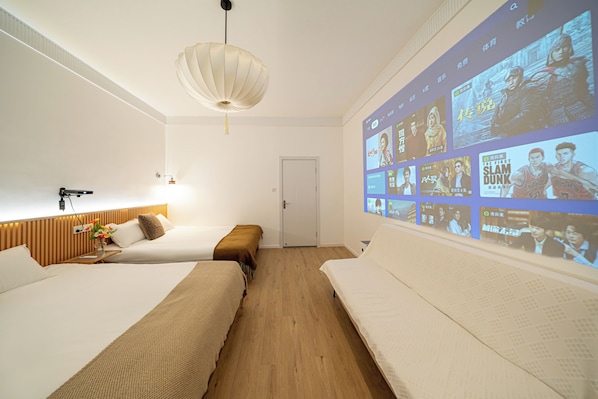 Une chambre d’hôtel avec deux lits, une tête de lit en bois, un téléviseur fixé au mur qui affiche des affiches de films, et un luminaire suspendu.