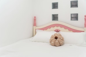 Una cama con sábana blanca, almohada y un peluche con lunares.