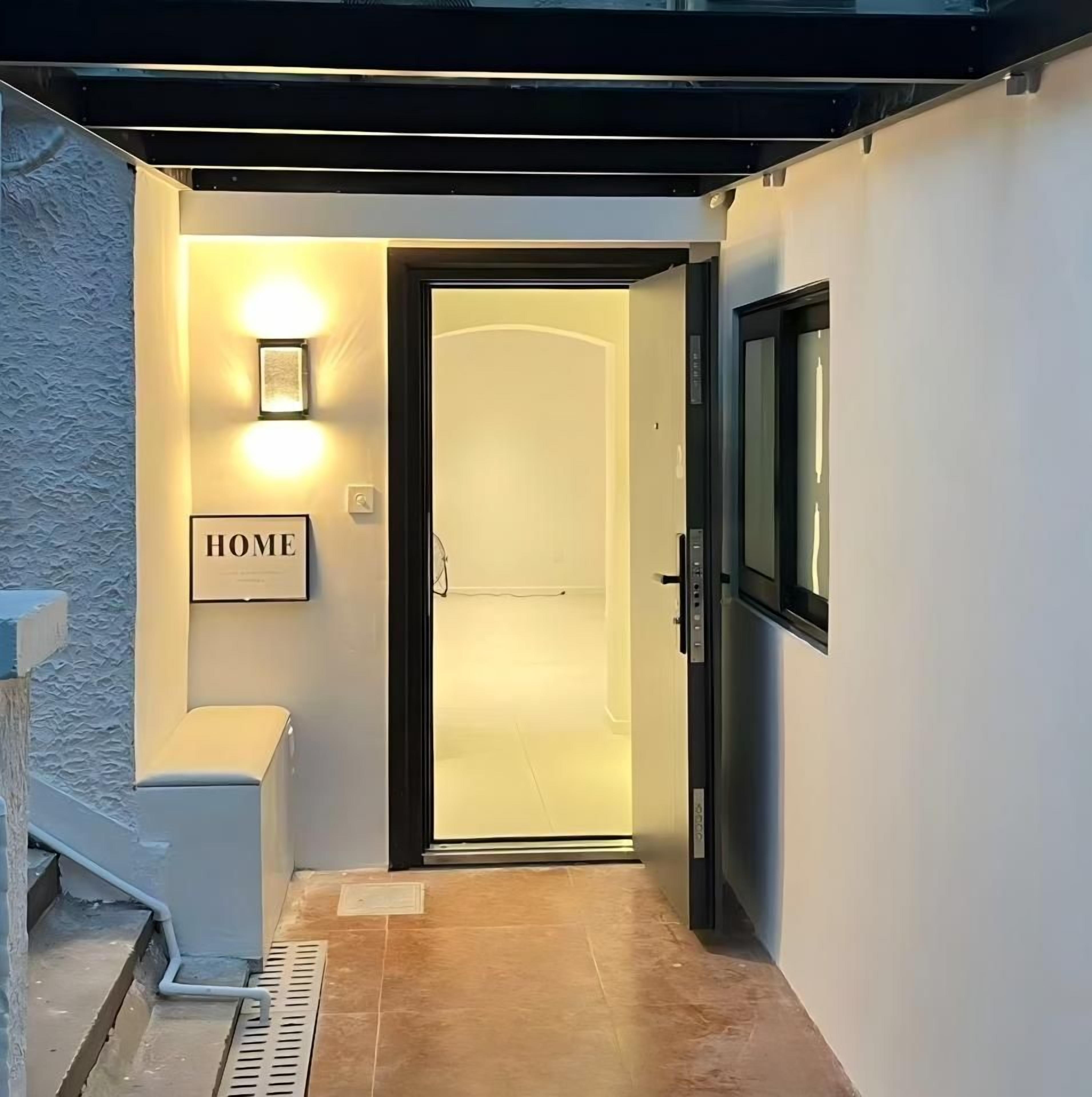 A modern entrance with a glass door, a wall-mounted light, and a 'HOME' sign.