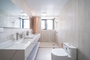 Et moderne badeværelse med et stort spejl, to håndvaske, en bruseniche og et toilet.