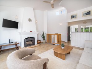 A living room with a fireplace, a television mounted on the wall, and a kitchen area visible through an open door. - Traditional House in Luz, Steps from the Beach (Luz, Lagos)