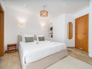 A bedroom with a large bed, bedside tables, a wooden door, and a wall-mounted light fixture. - Traditional House in Luz, Steps from the Beach (Luz, Lagos)