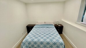 Een slaapkamer met een bed, twee nachtkastjes, een raam met zonwering en inbouwspots.
