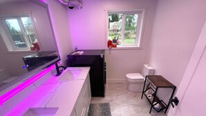 Een kleine badkamer met een witte marmeren wastafel, een zwart kastje, een toilet en een klein houten tafeltje.
