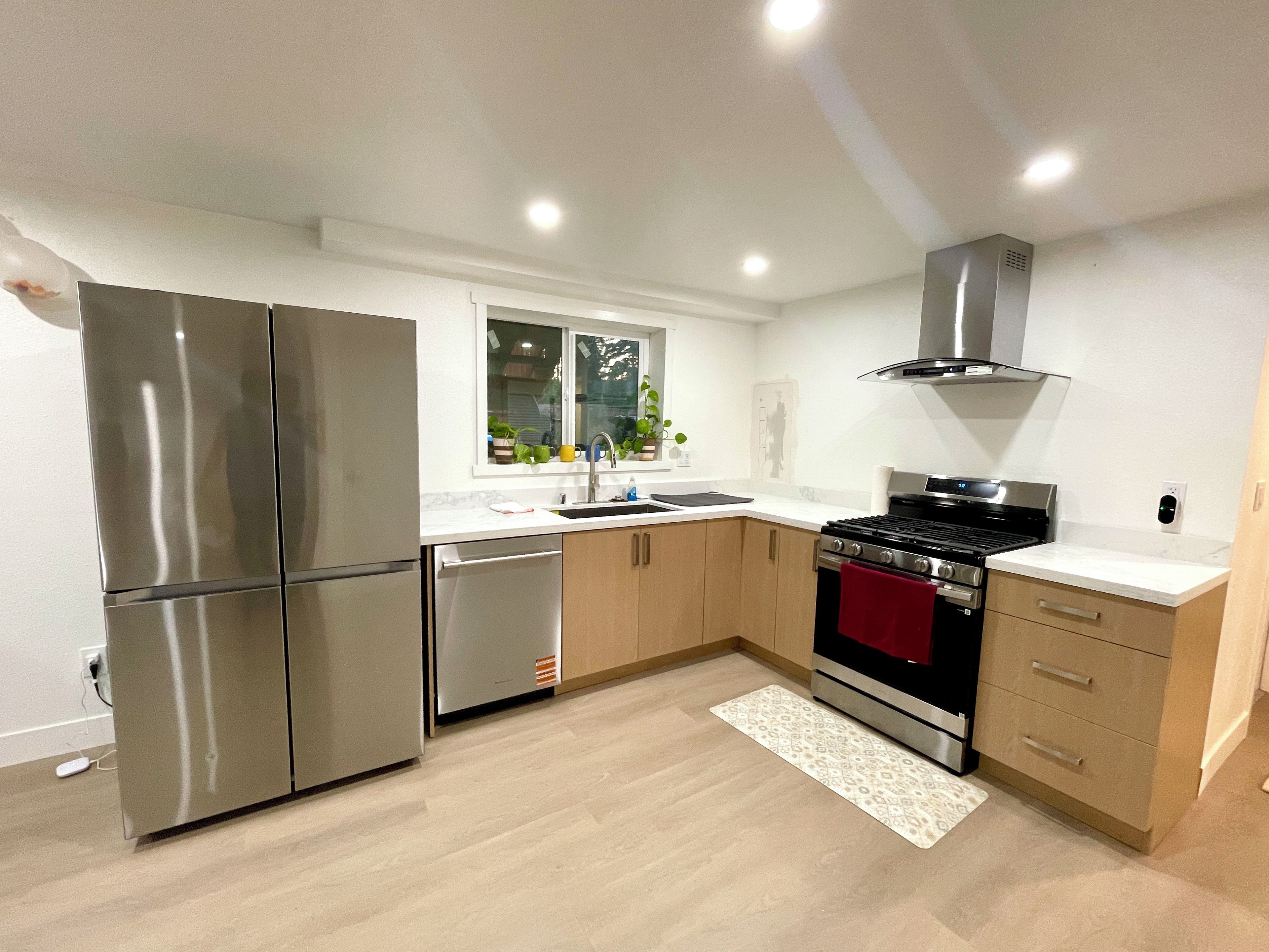 A modern kitchen with stainless steel appliances, a window with plants, and a red towel on the oven.
