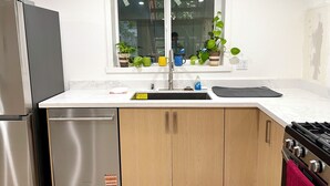 Een keuken met een roestvrijstalen koelkast, een vaatwasser, houten kastjes, een raam met potplanten en een zwart aanrecht.