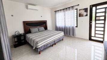 A bedroom with a bed, a bedside table, a wall-mounted air conditioner, and a door with a view.
