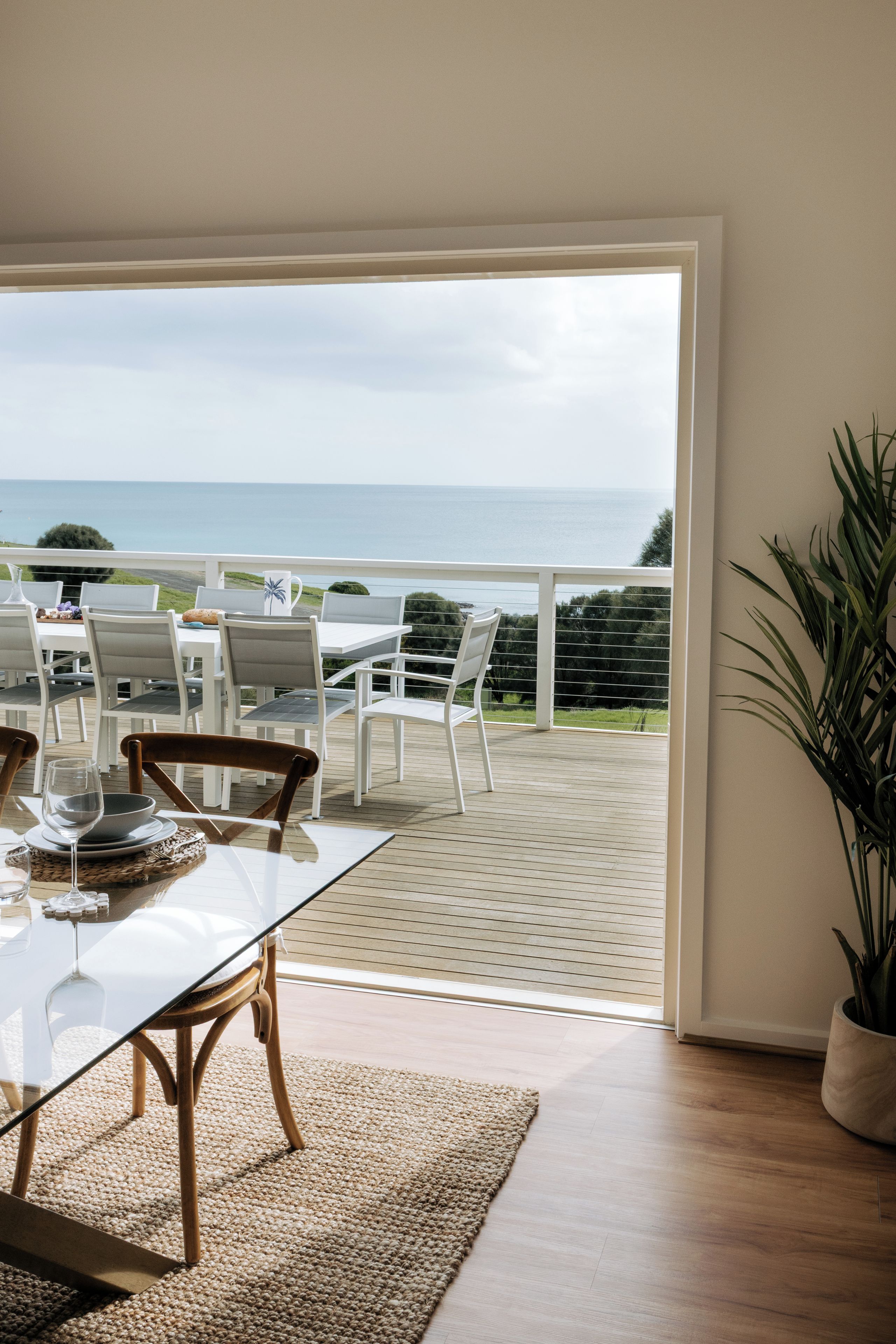 Un comedor con vistas al mar, con una mesa y sillas, una mesa de vidrio y una planta en maceta.