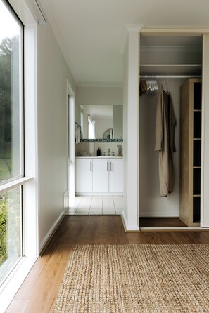 Ein modernes Interieur mit Holzboden, einem weißen Badezimmer mit Fliesenrückwand und einem begehbaren Kleiderschrank mit Kleidung.