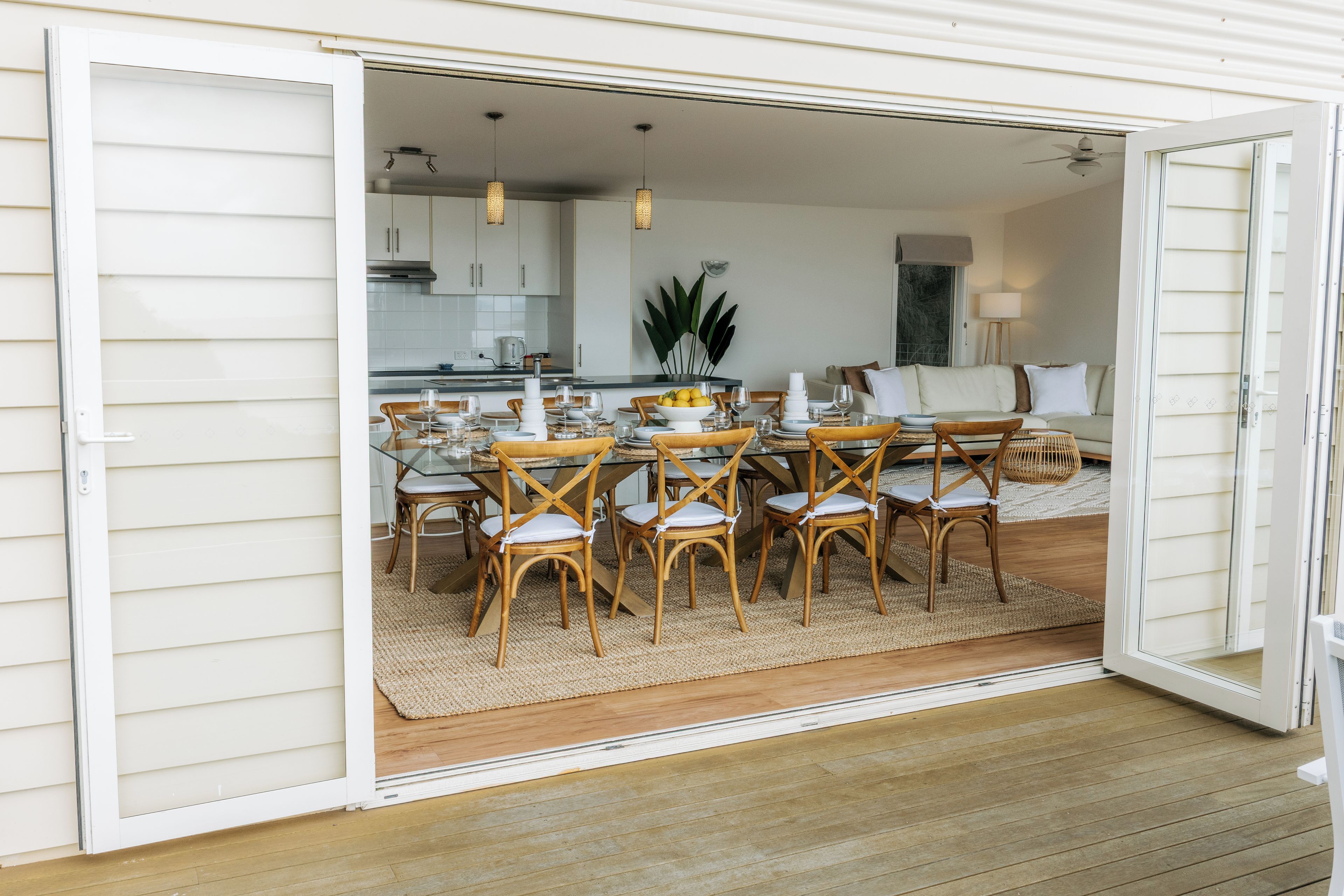 An open sliding door leading to a dining area with a glass table, wicker chairs, and a kitchen in the background.
