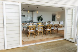An open sliding door leading to a dining area with a glass table, wicker chairs, and a kitchen in the background. - Oracle Beach House @ Penneshaw, Kangaroo Island (Penneshaw)