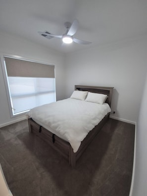 A bedroom with a bed, a ceiling fan, and a window with blinds.