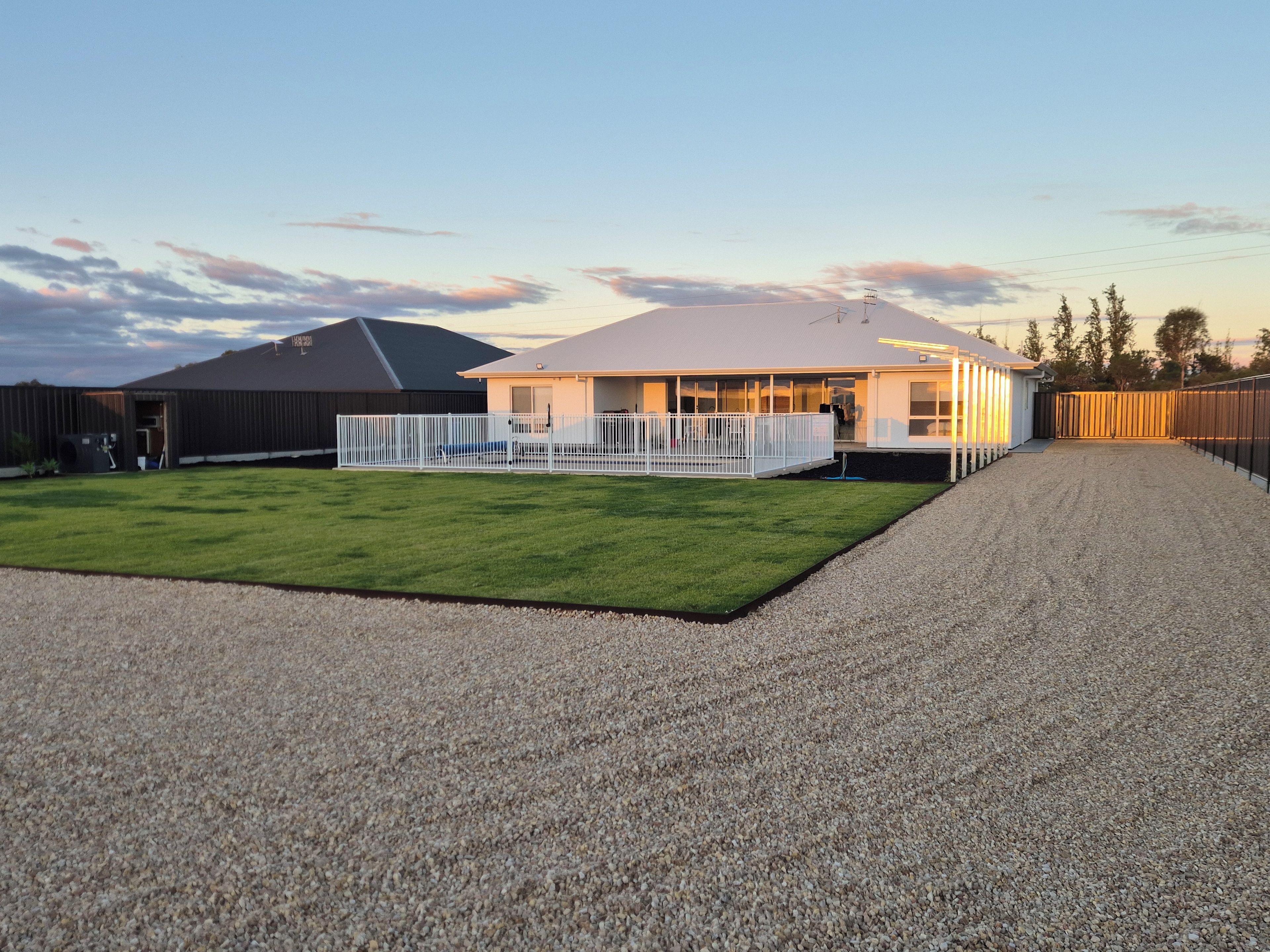 A house with a covered patio, a fenced yard, and a gravel driveway.