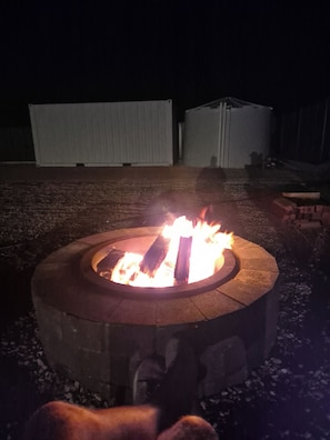 A circular outdoor fire pit with burning logs, surrounded by gravel.