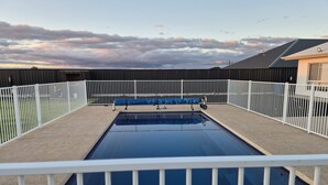 A rectangular swimming pool with a white fence surrounding it, set against a backdrop of a cloudy sky.