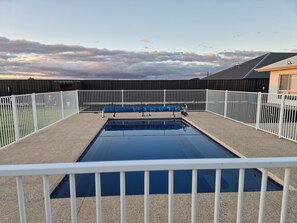 A rectangular swimming pool with a white fence surrounding it, set against a backdrop of a cloudy sky. - Paringa Escape (Paringa)