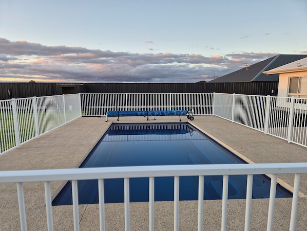 A rectangular swimming pool with a white fence surrounding it, set against a backdrop of a cloudy sky.