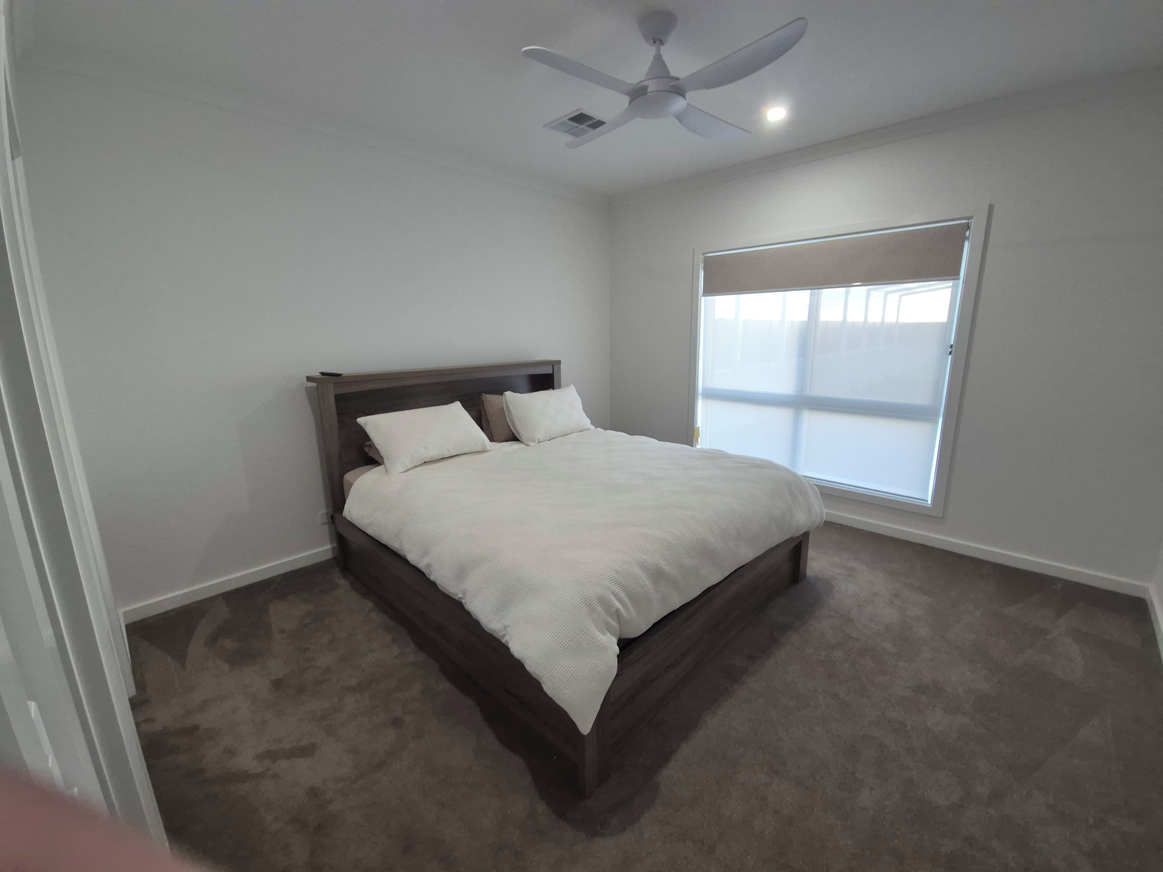 A bedroom with a bed, a ceiling fan, and a window with blinds.