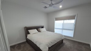 A bedroom with a bed, a ceiling fan, and a window with blinds.