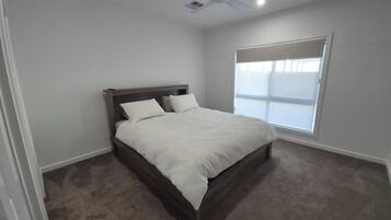 A bedroom with a bed, a ceiling fan, and a window with blinds.