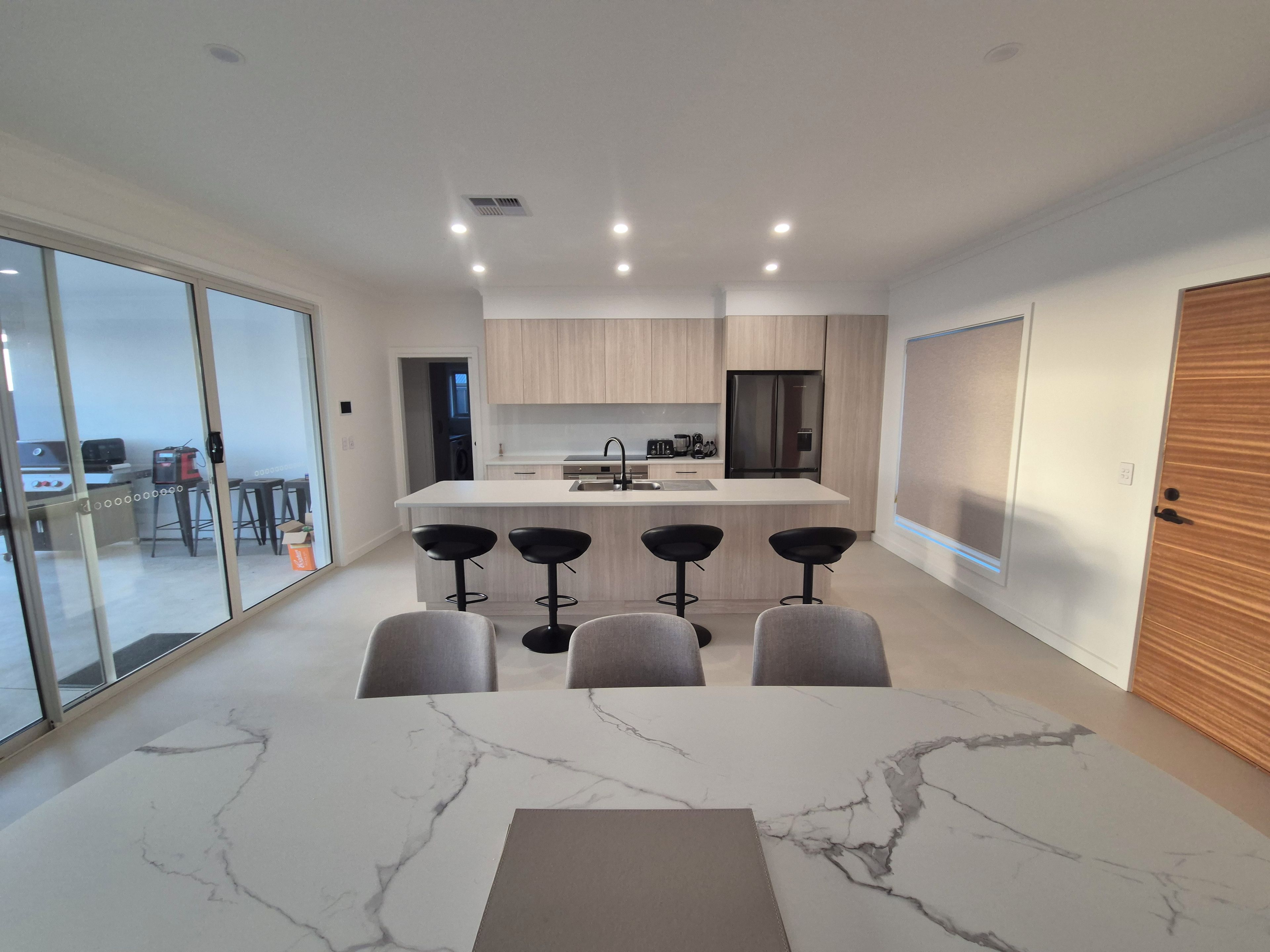 A modern kitchen with a central island, bar stools, and a dining area with a marble table.