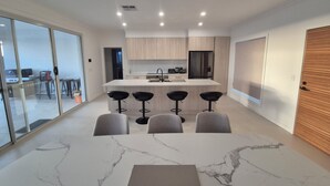A modern kitchen with a central island, bar stools, and a dining area with a marble table.
