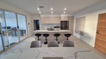 A modern kitchen with a central island, bar stools, and a dining area with a marble table.