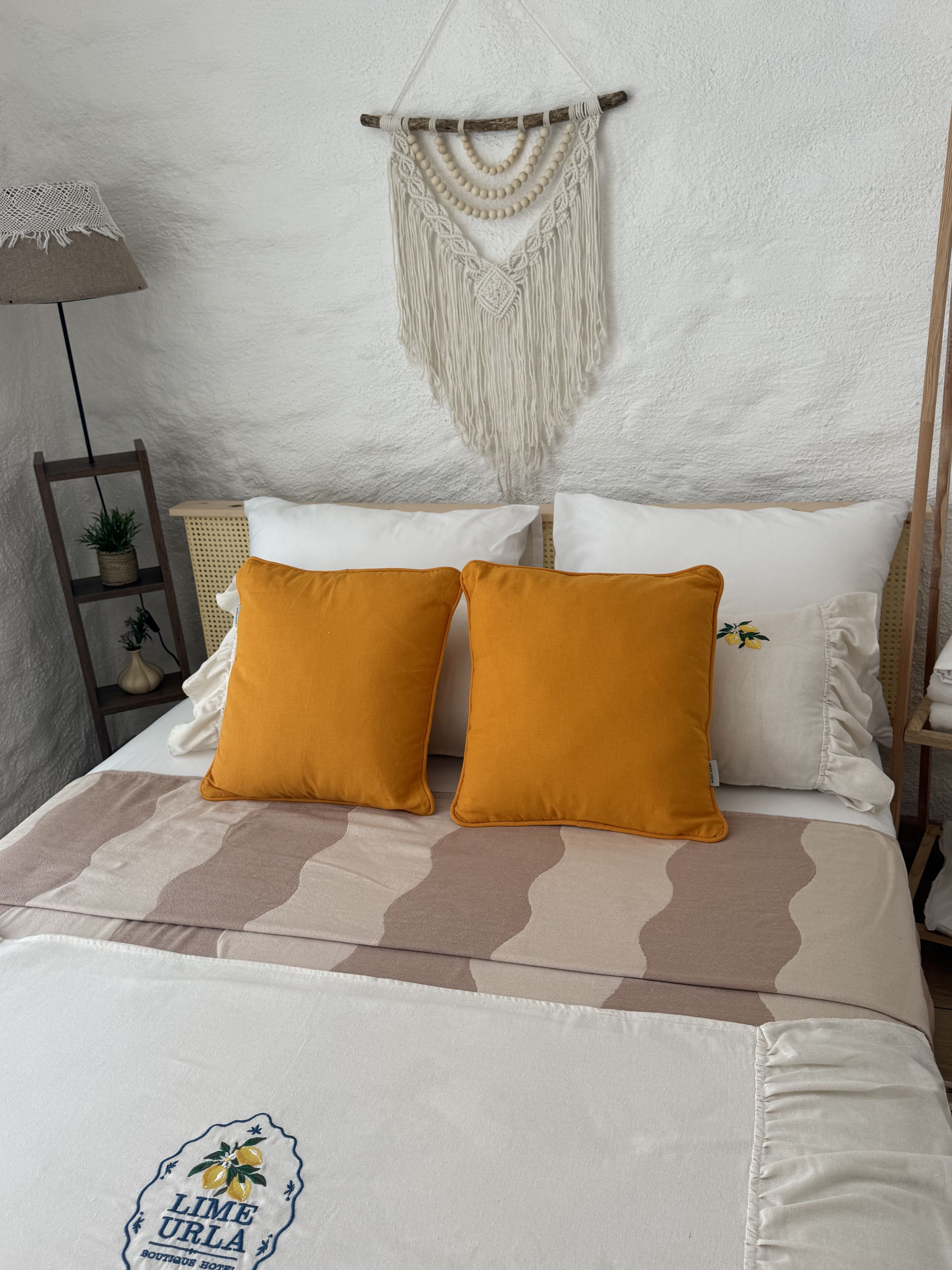 A bed with two mustard pillows, a macrame wall hanging, and a small shelf with plants.