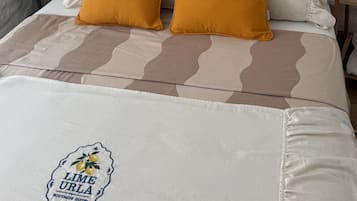 Una cama con dos almohadones mostaza, un tapiz de macramé y un estante pequeño con plantas.