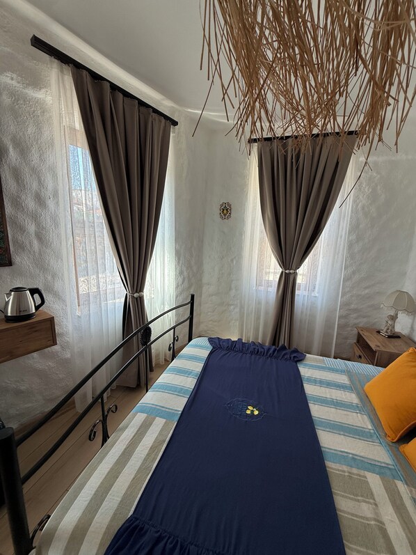 A bedroom with a bed, a nightstand, a wooden shelf, a window with curtains, and a hanging plant. - Urla Lime Hotel (Urla)