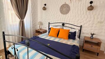 Un dormitorio con estructura metálica para la cama, una colcha a rayas y dos mesitas de noche con lámparas.
