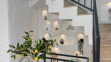Un escalier avec une rampe noire, un mur blanc orné d’éléments décoratifs et une table sur laquelle est posé un vase rempli de citrons.