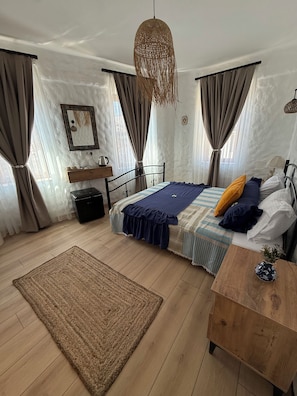 A bedroom with a bed, a bedside table, a hanging light fixture, a window with curtains, and a wall-mounted shelf with a kettle. - Urla Lime Hotel (Urla)