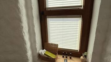 A room with a window, a wicker basket, a roll of toilet paper, and a small plant.